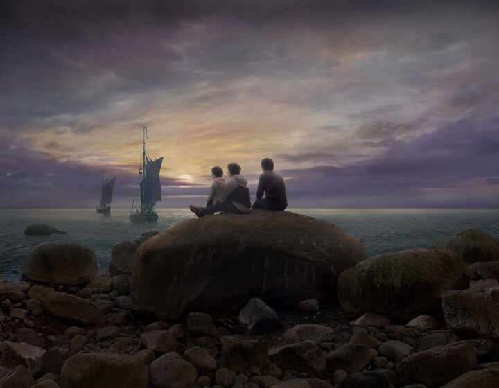 Im Vordergrund des Bildes ist ein großer Felsen zu sehen, auf dem drei Personen sitzen. Sie schauen auf das vor ihnen liegende Meer, auf dem zwei Segelboote schwimmen. Am Horizont geht der Mond auf.