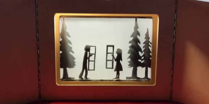 Auf dem Foto ist eine Schattentheaterbühne zu erkennen, auf der zwei Figuren: ein Mädchen und ein Junge jeweils an einem Fenster stehen. An den Seiten stehen Bäume.   &copy;Romantikerhaus Jena
